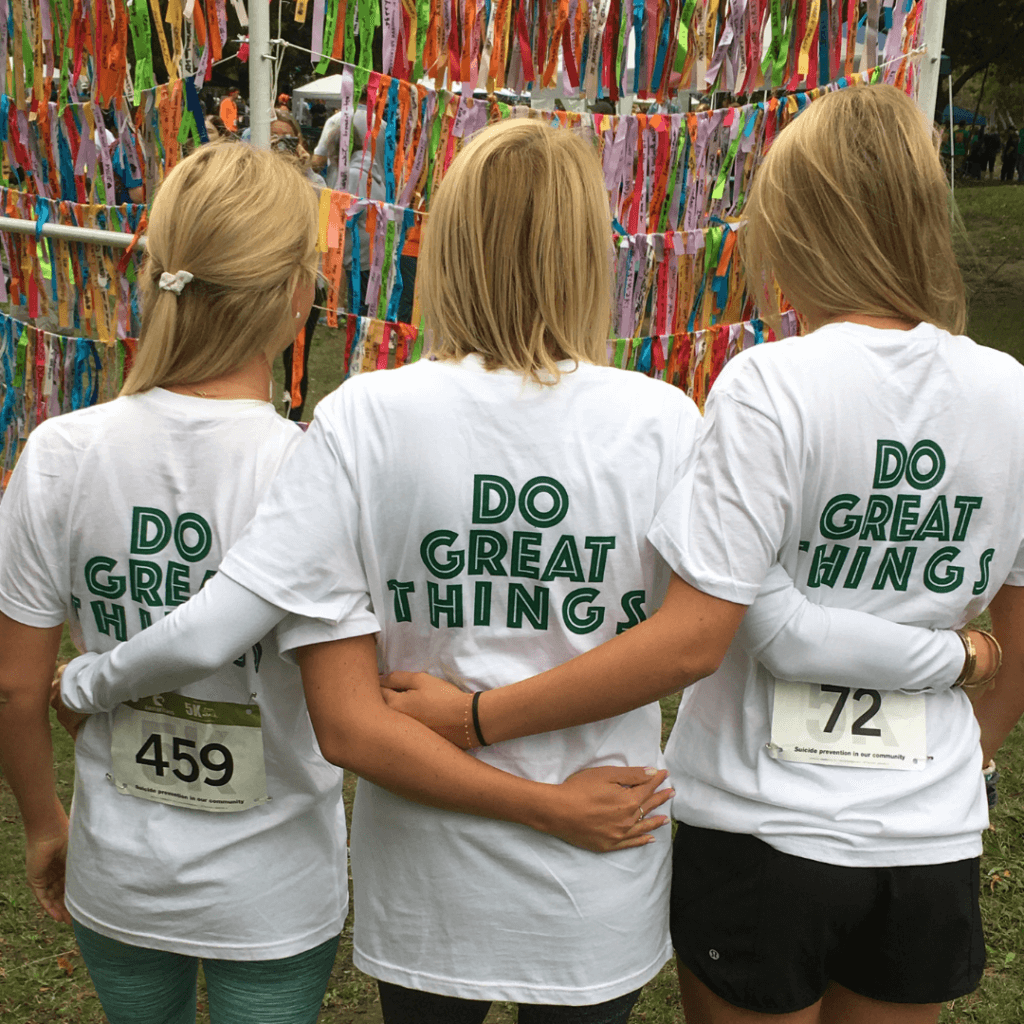 The backs of three people who are wearing white t-shirts that say Do Great Things