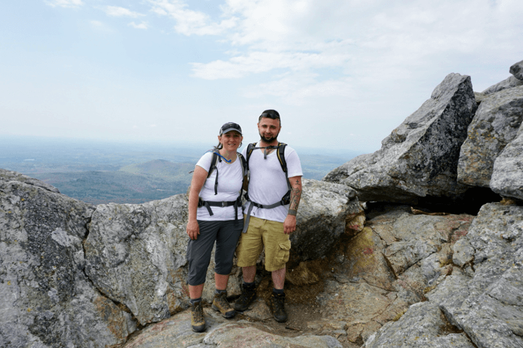 two people stand on a mountaintop smiling