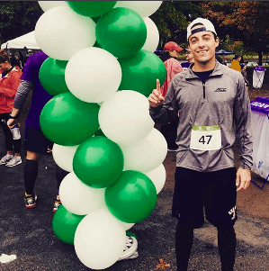 Man smiles and holds up one finger in front of balloons at Samaritans 5K.
