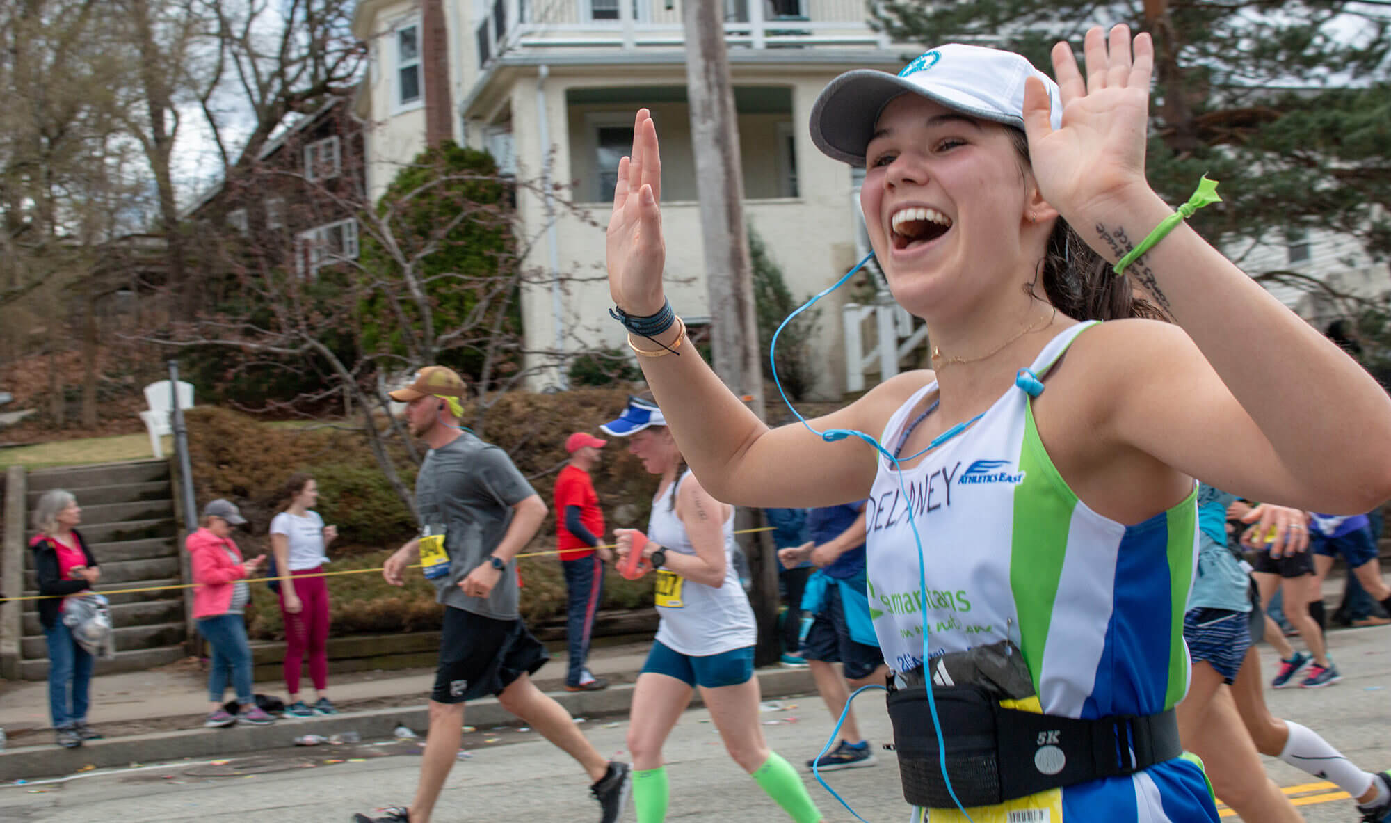 A person smiling with her hands up while running in a race.