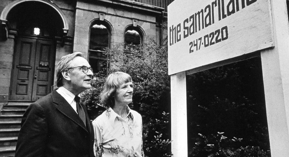Two people stand next to a Samaritans sign.