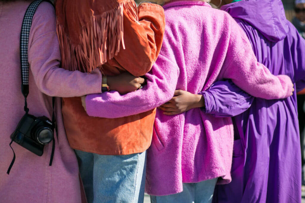 A group of women in pink and purple jackets embracing. 