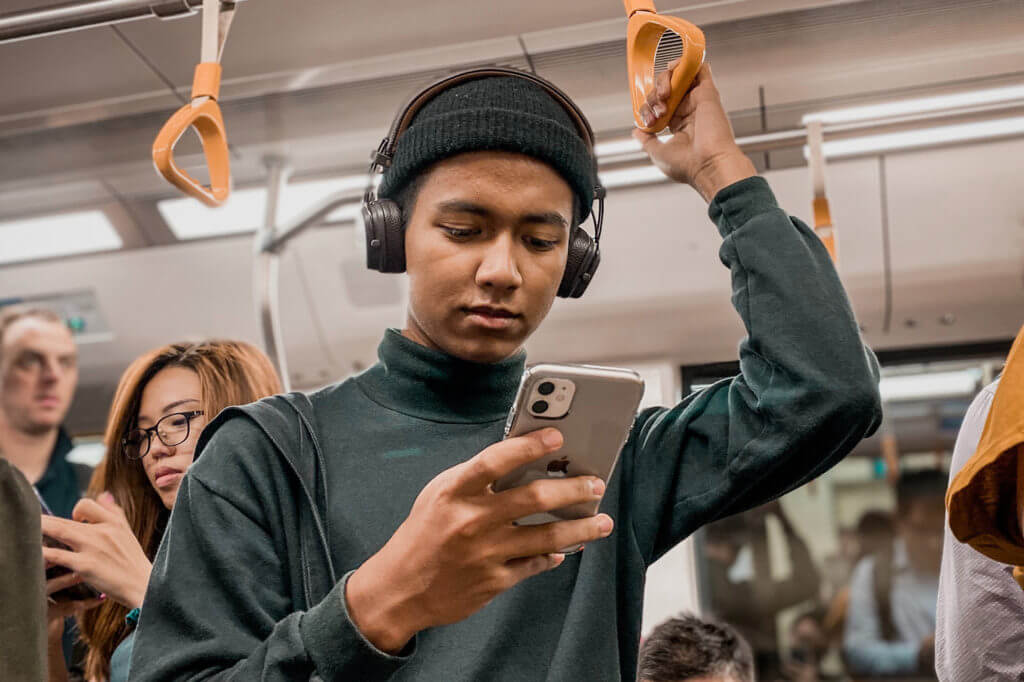Man wearing headphone and looking at this phone on a public transportation.