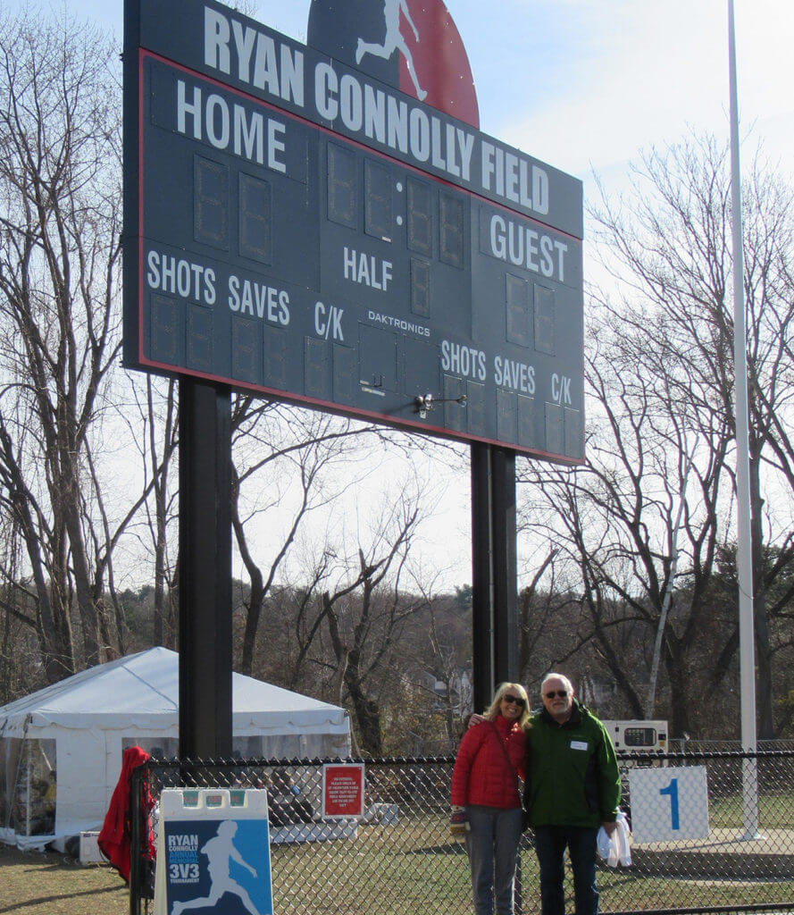 Two people standing below a soccer field score board