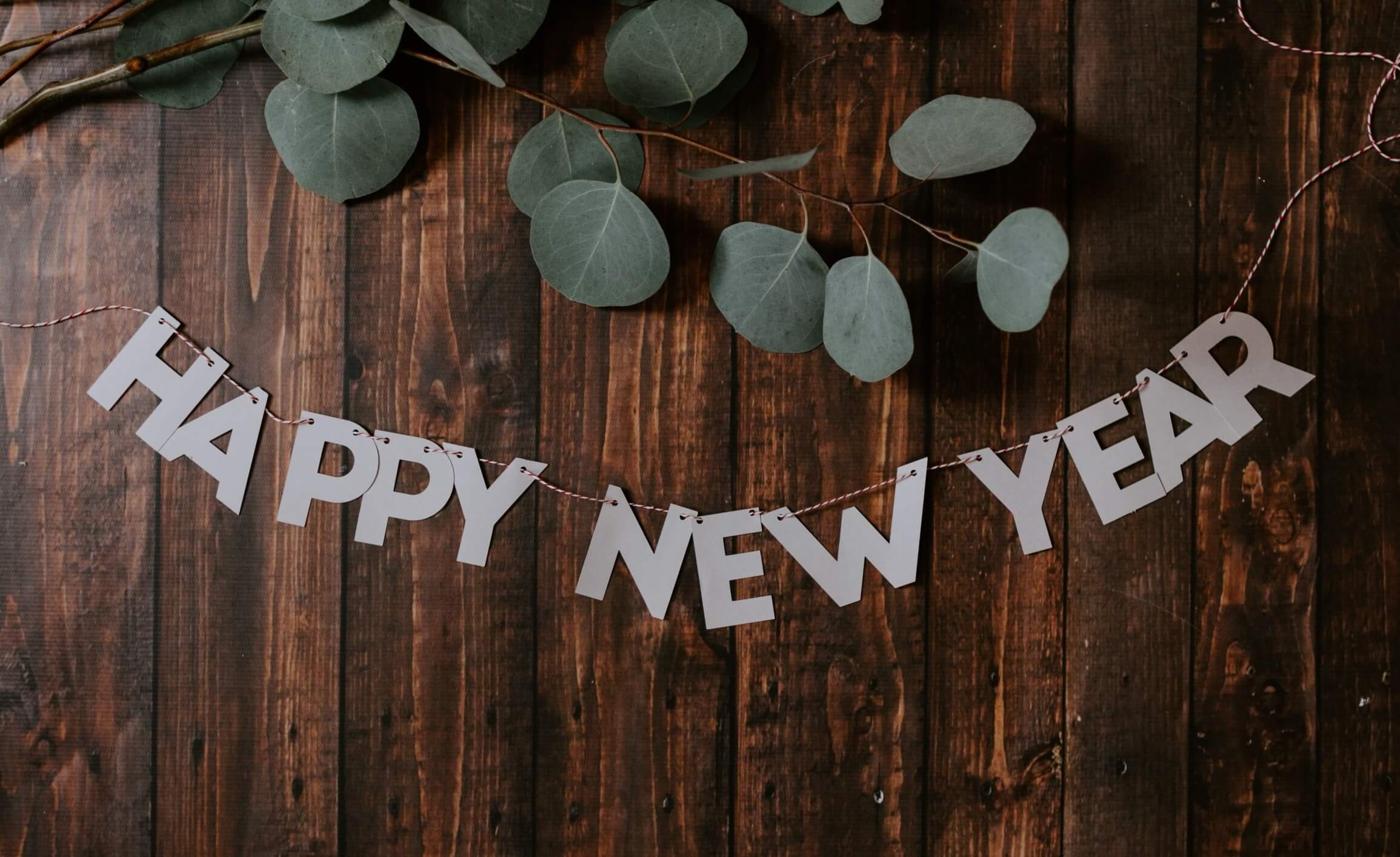 wood background with banner that says HAPPY NEW YEAR accented by some leaves
