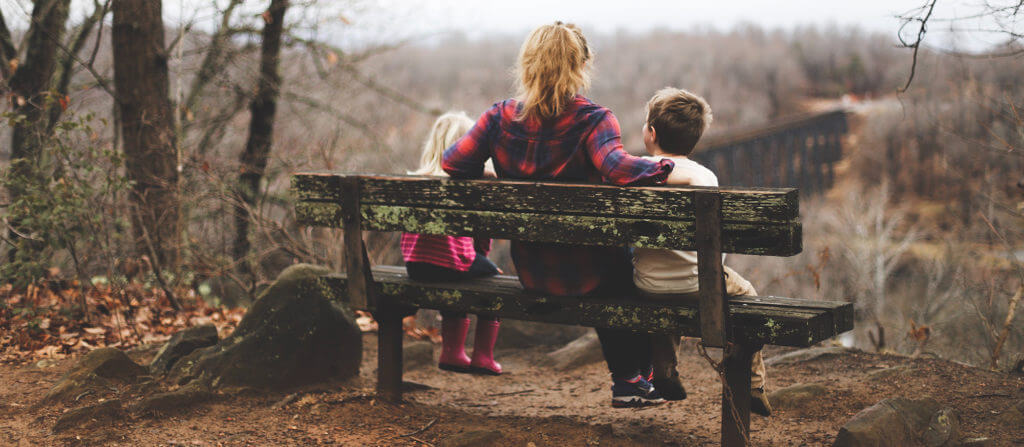 A mother and her two children sitting on a bench.