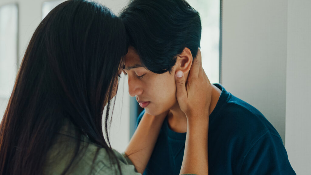 A girlfriend comforting her suicidal boyfriend. Their heads are pressed together and her hands are holding his face.