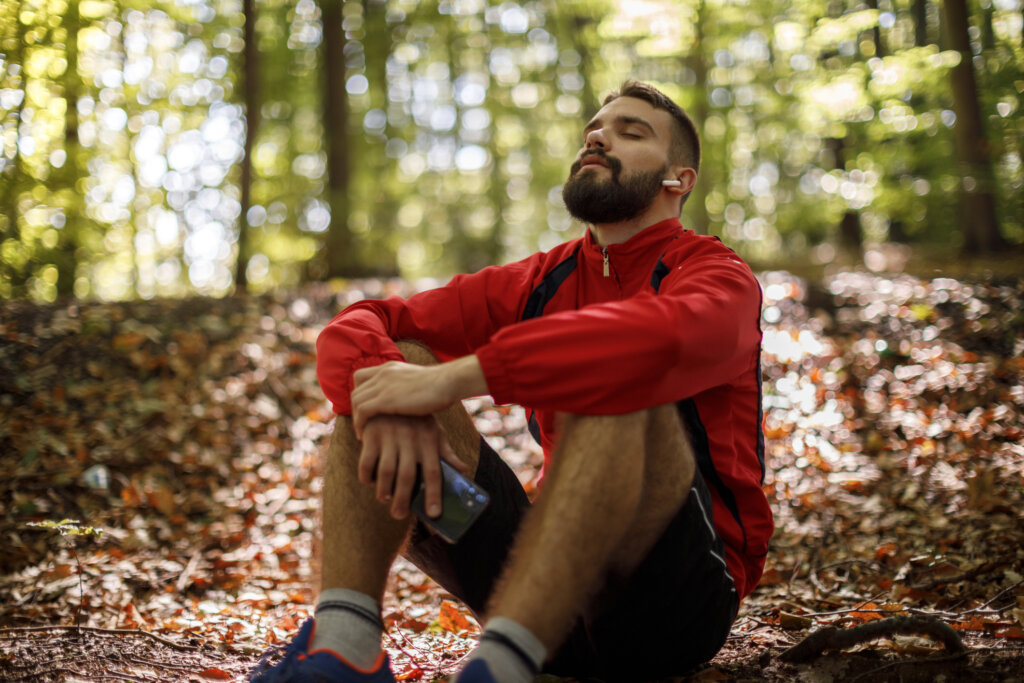 A man practicing self-care to help him stop feeling suicidal by sitting in the woods with his headphones on