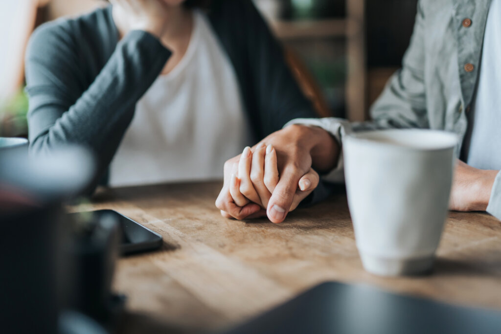 Two people sitting at a table together holding hands