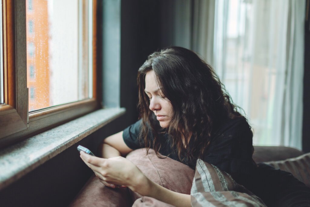 A depressed woman who's feeling suicidal is sitting by the window on her iPhone